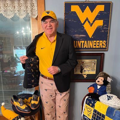 WVU male fan with gold polo and khaki Flying WV pants with other WVU memorabilia in background