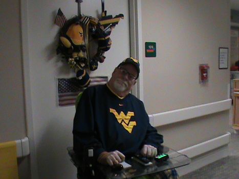 Male WVU fan with Navy Flying WV sweatshirt sitting in wheelchair in front of door